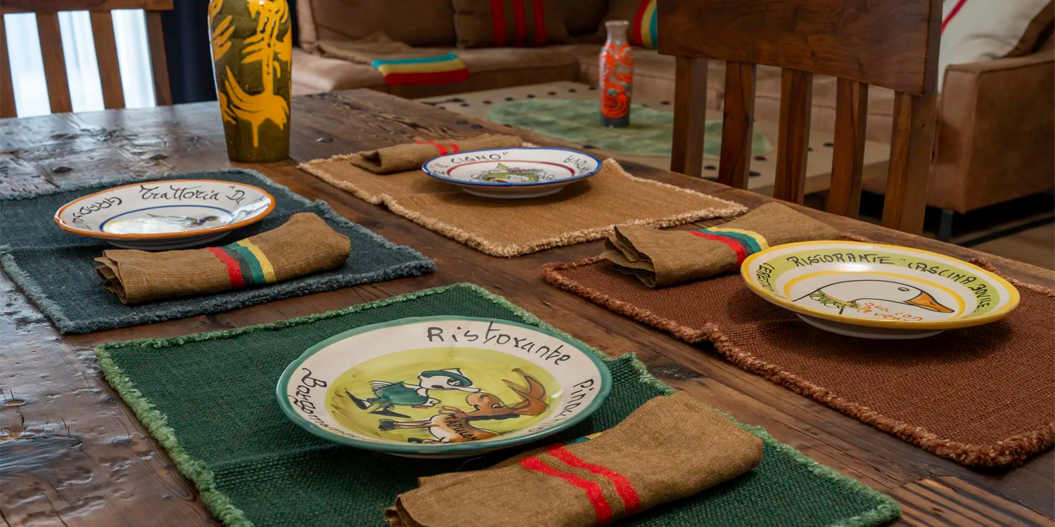 Rustic dining table setting with hand-painted Buon Ricordo Italian ceramic plates, vintage woven placemats, and linen napkins. Elegant Mediterranean-inspired home decor by Gordina.