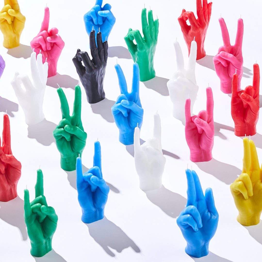 Colorful hand-shaped candles in various gestures, arranged on a white background. Unique sculptural wax candles by Gordina, blending art and home decor.