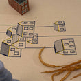 Load image into Gallery viewer, Handmade embroidered cotton tablecloth featuring connected houses, designed to evoke warmth and togetherness.