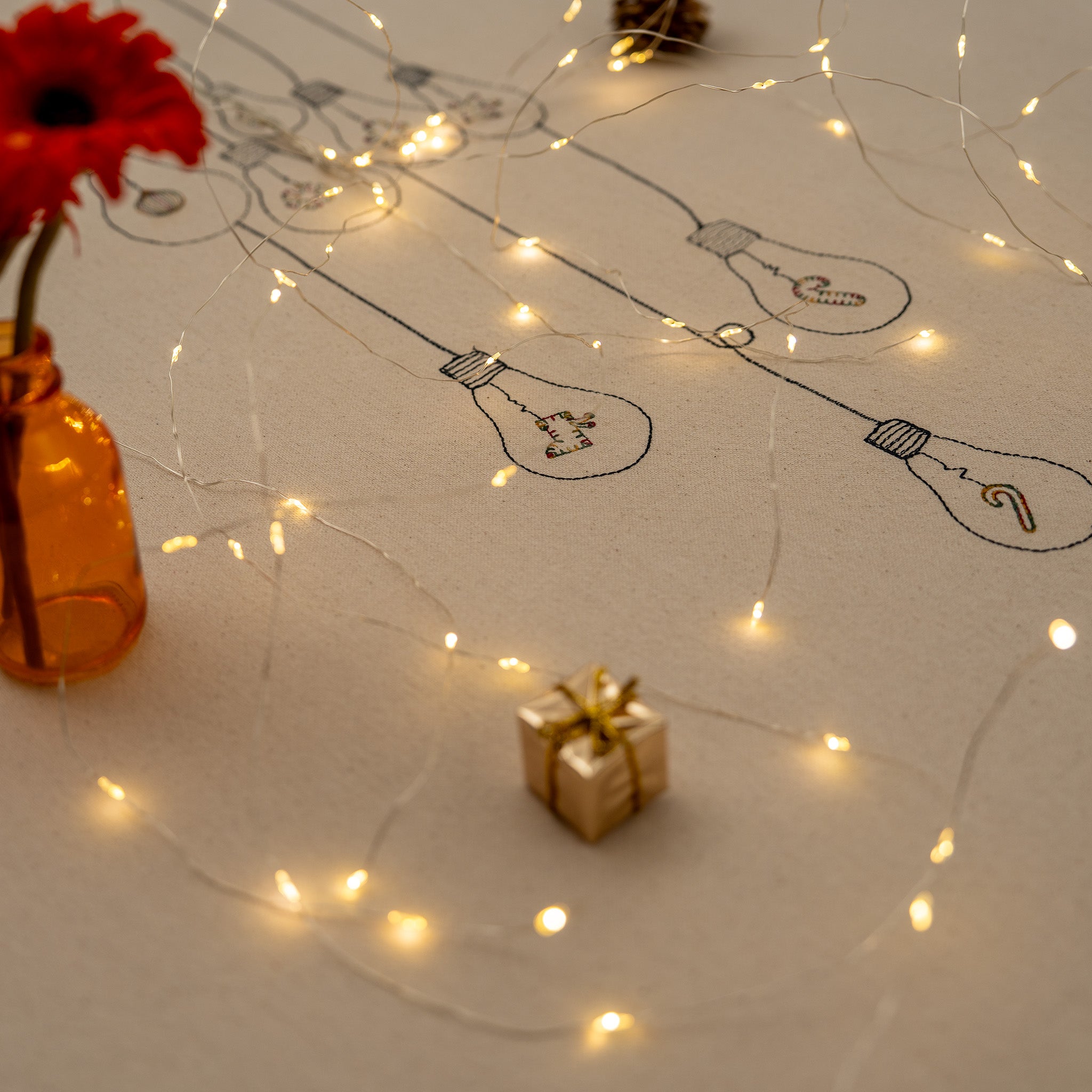 Handmade embroidered cotton tablecloth with festive light bulb design, crafted in the Netherlands for holiday gatherings.
