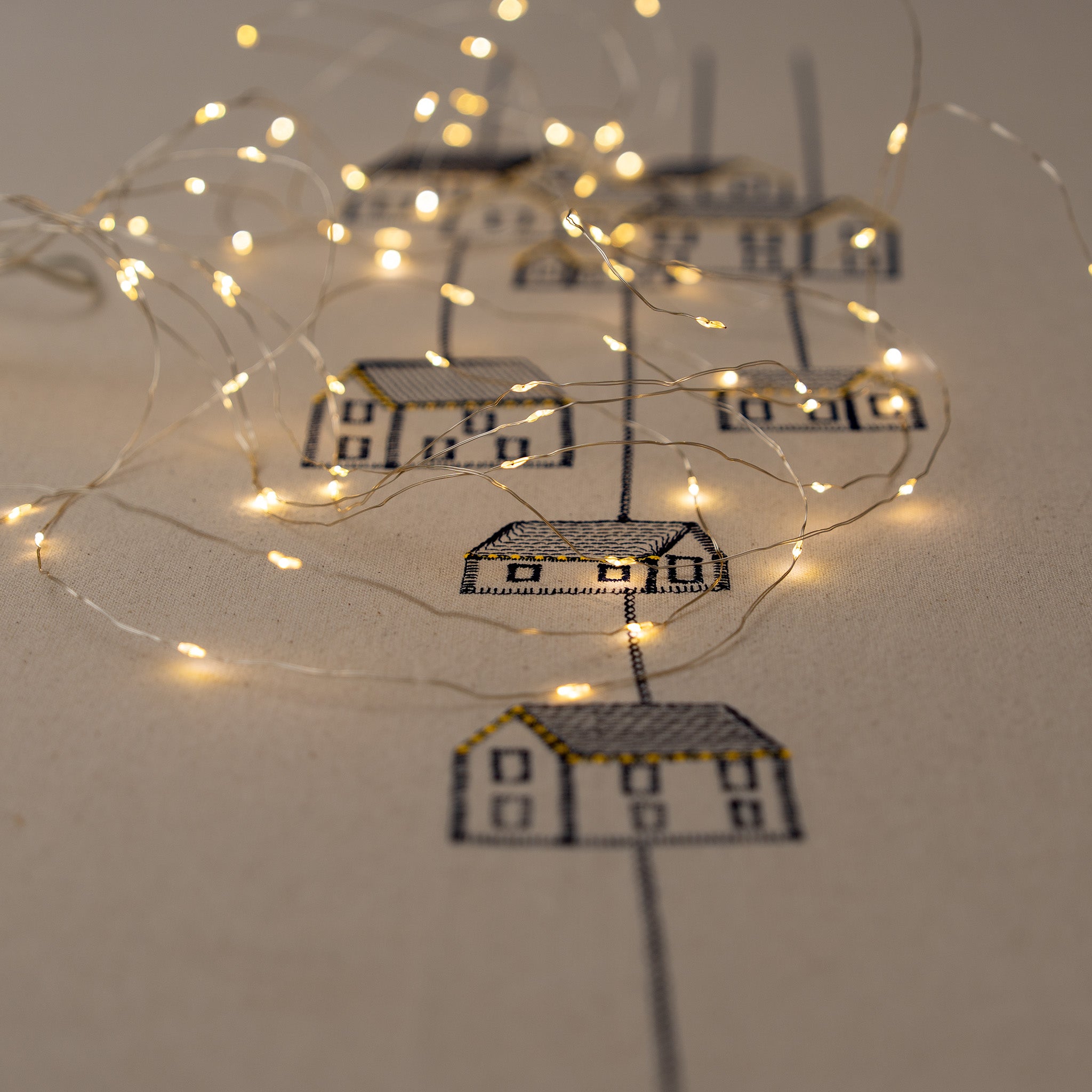 Handmade embroidered cotton tablecloth featuring connected houses, designed to evoke warmth and togetherness.