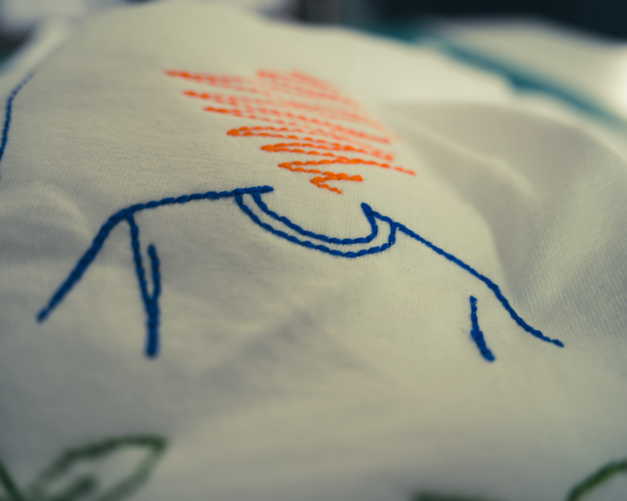 Embroidered t-shirt detail by Gordina, organic cotton fabric with blue and orange thread, minimal wearable art design