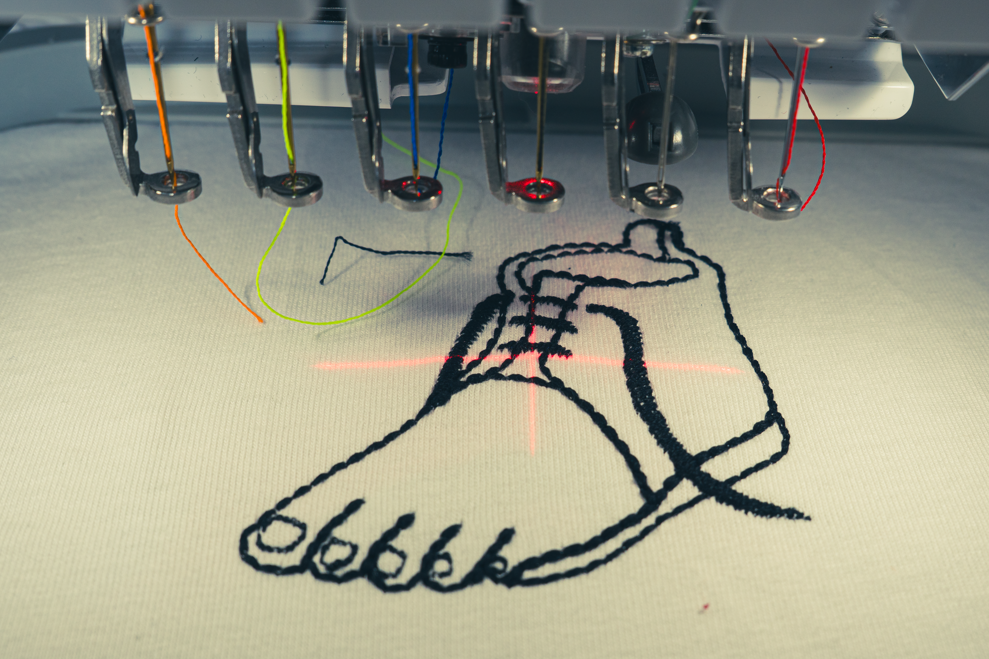 Close-up of embroidery machine creating a line art shoe design on cotton fabric, Gordina embroidered t-shirt production process