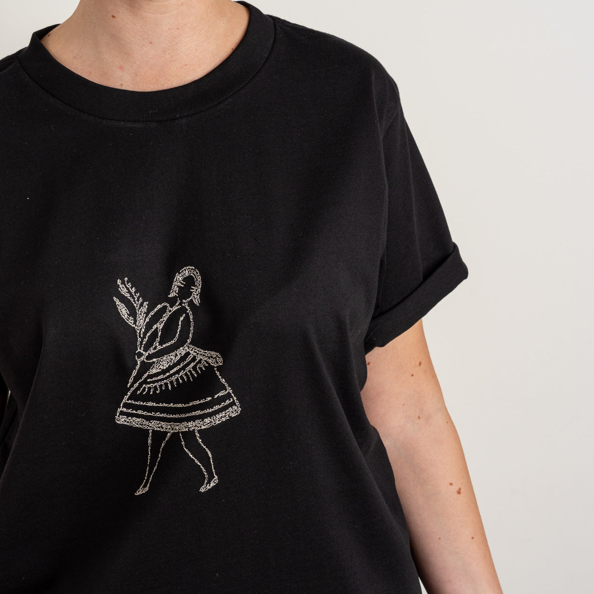 Close-up of the cream dancing-figure embroidery on the Black La Bailarina T-shirt.