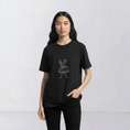 Load image into Gallery viewer, Model wearing the La Bailarina black T-shirt with a cream-thread dancing figure embroidered at the centre chest
