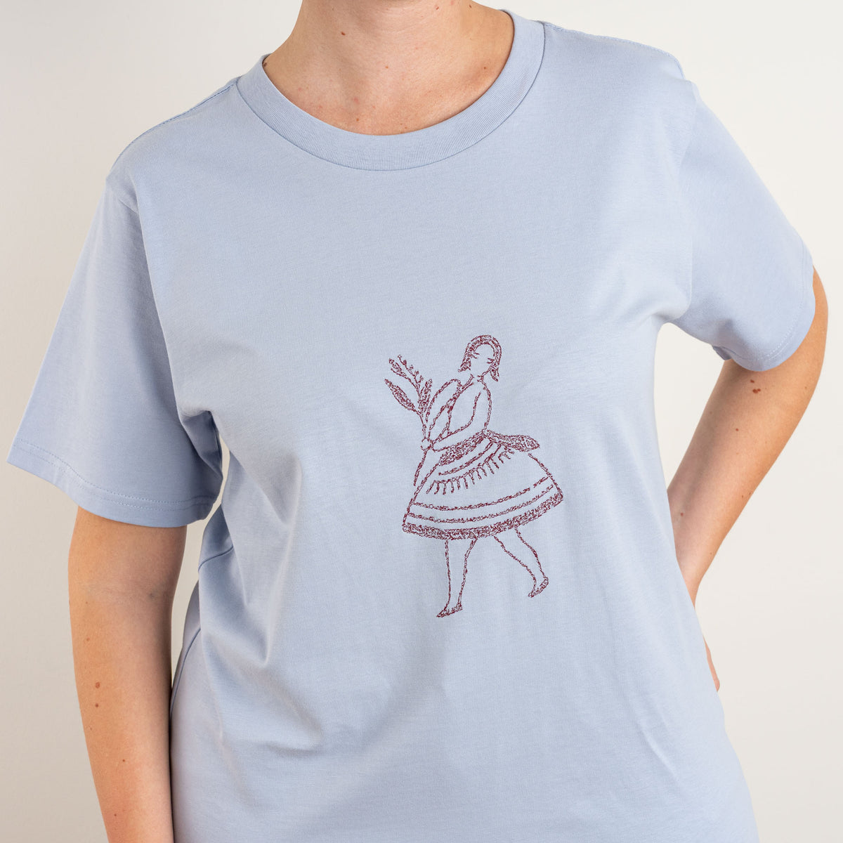 Close detail of the burgundy dancing-figure embroidery on Gordina’s Powder La Bailarina T-shirt.