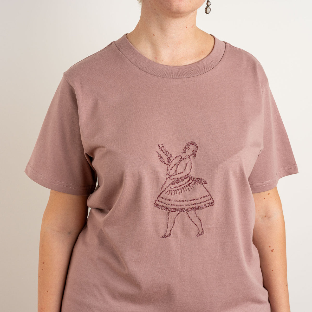 Close-up of the dark dancing-figure embroidery on Gordina’s Terracotta La Bailarina T-shirt.
