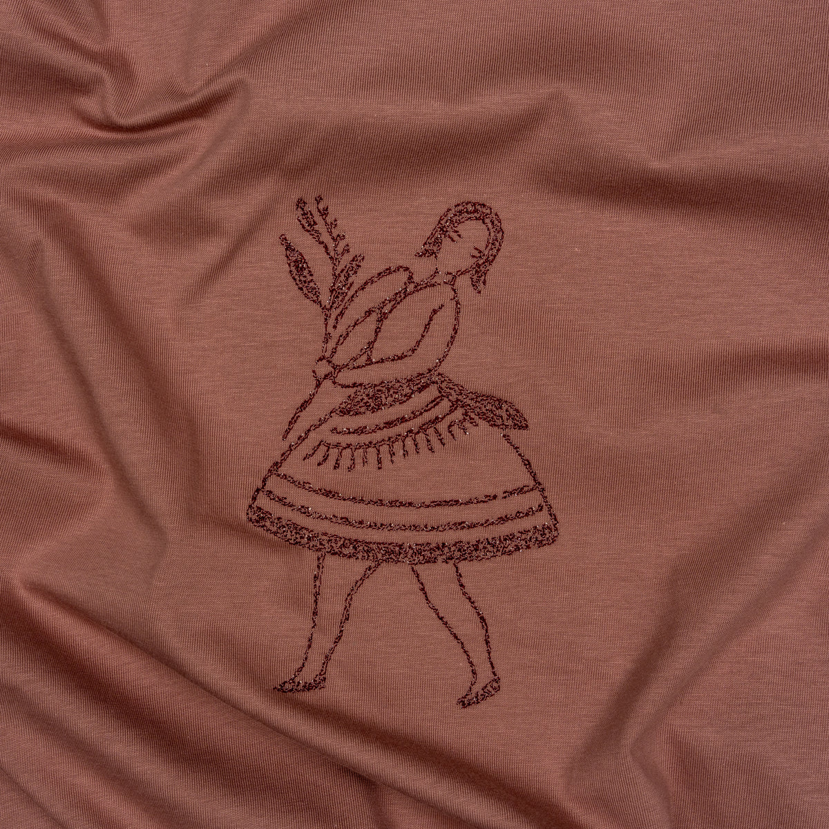 Close-up of dark-thread embroidery on the La Bailarina terracotta T-shirt, showing the dancer and flower branch