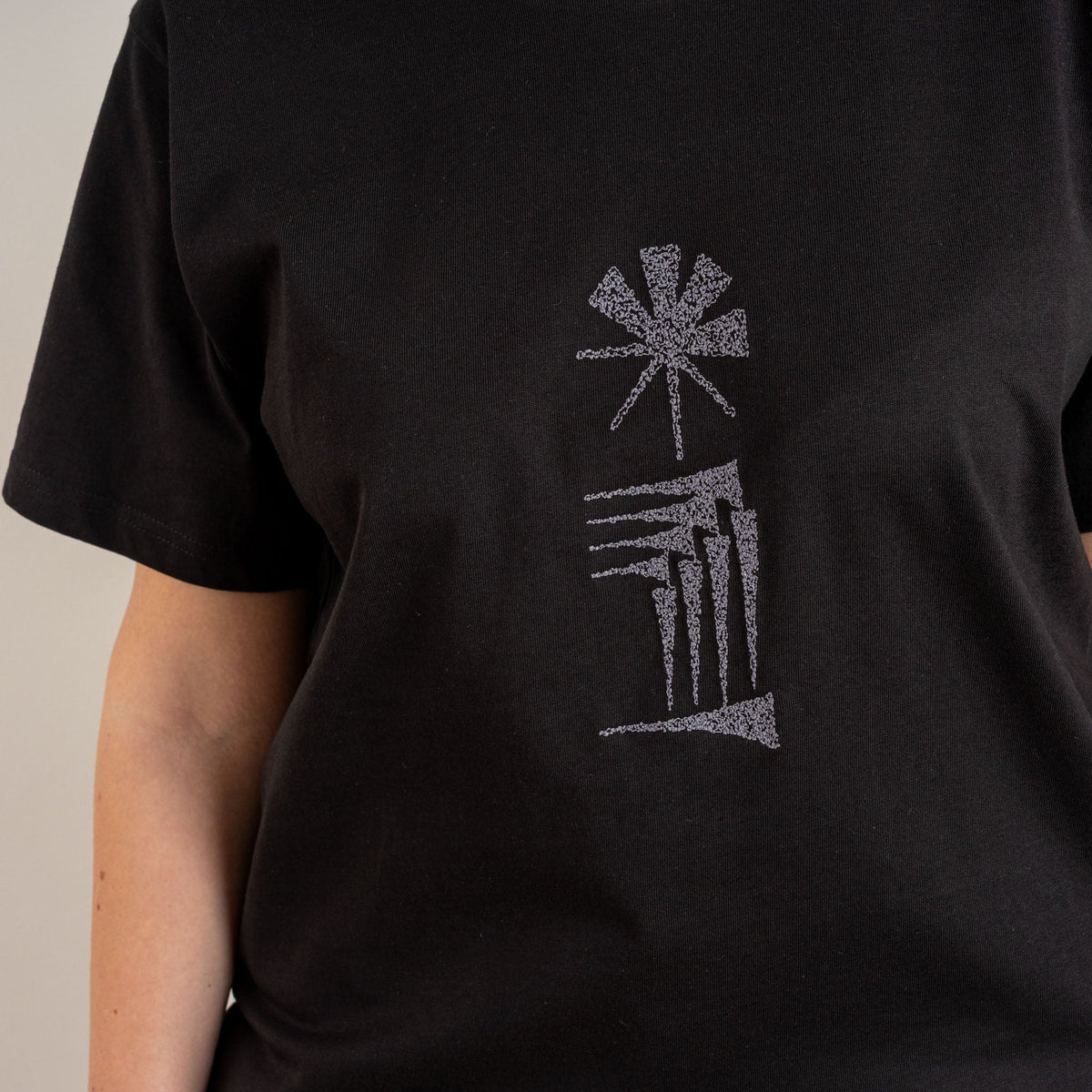 Close-up detail of the grey Star and House embroidery on the black women’s cotton T-shirt, photographed for Gordina in the Netherlands.