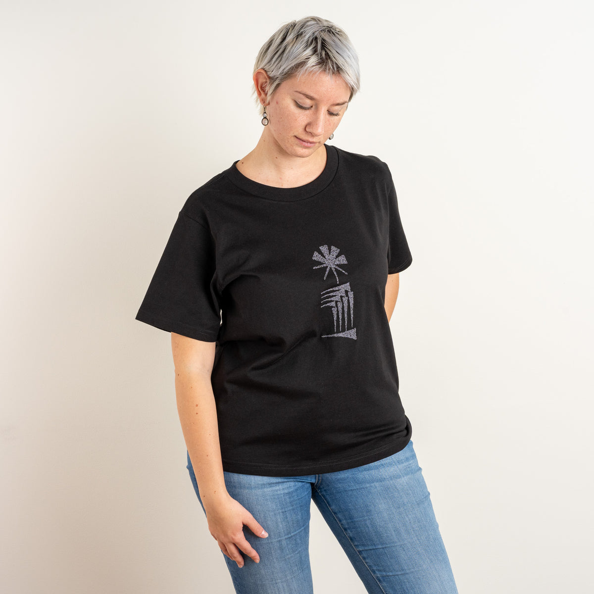 Model looking down while wearing the women’s black Star and House T-shirt with chest embroidery.