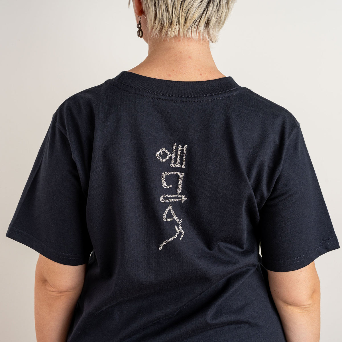 Close-up of the white Papyrus embroidery on the upper back of Gordina’s navy T-shirt, embroidered in the Netherlands.