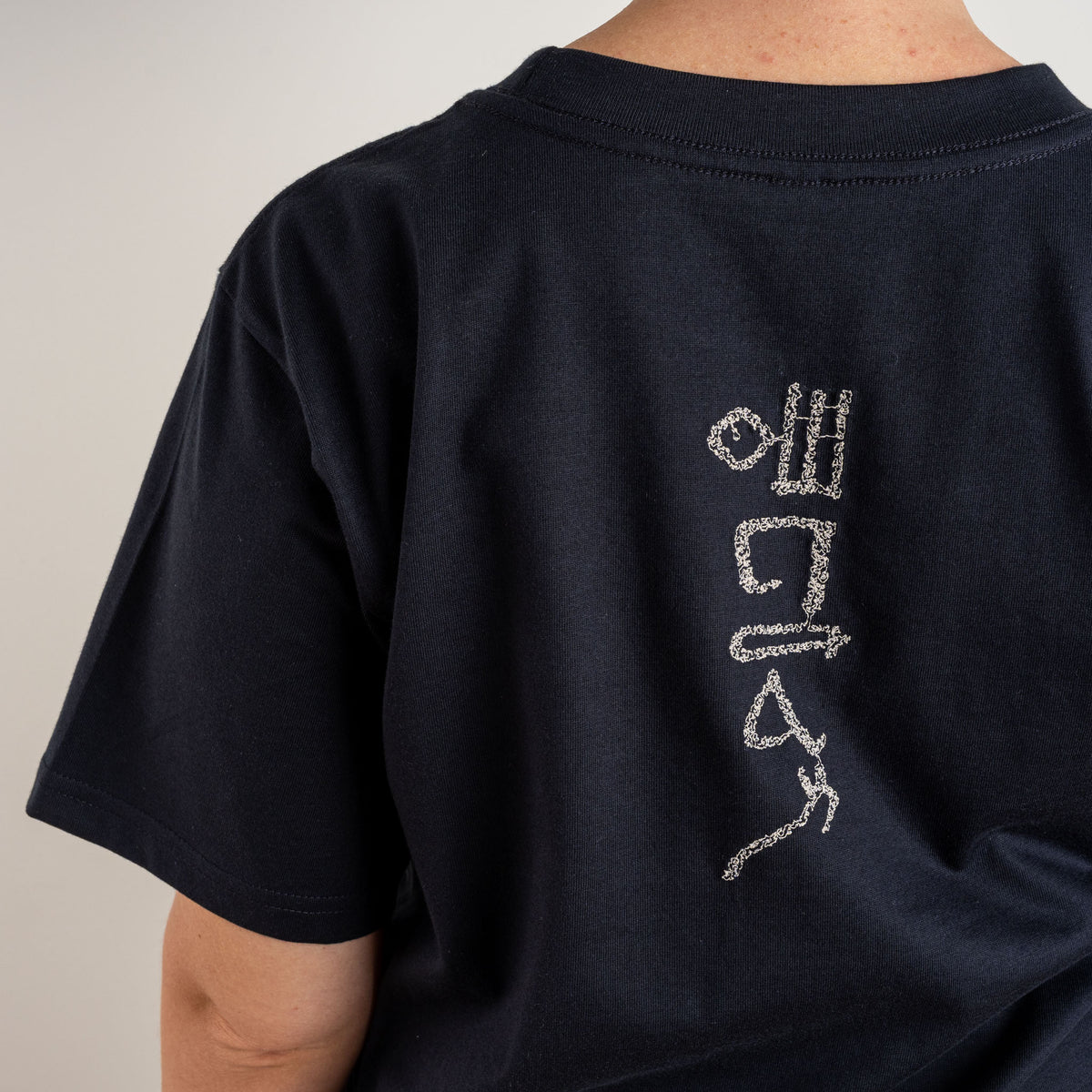 Detailed view of the white Papyrus motif stitched on navy cotton, from Gordina’s embroidered T-shirt.