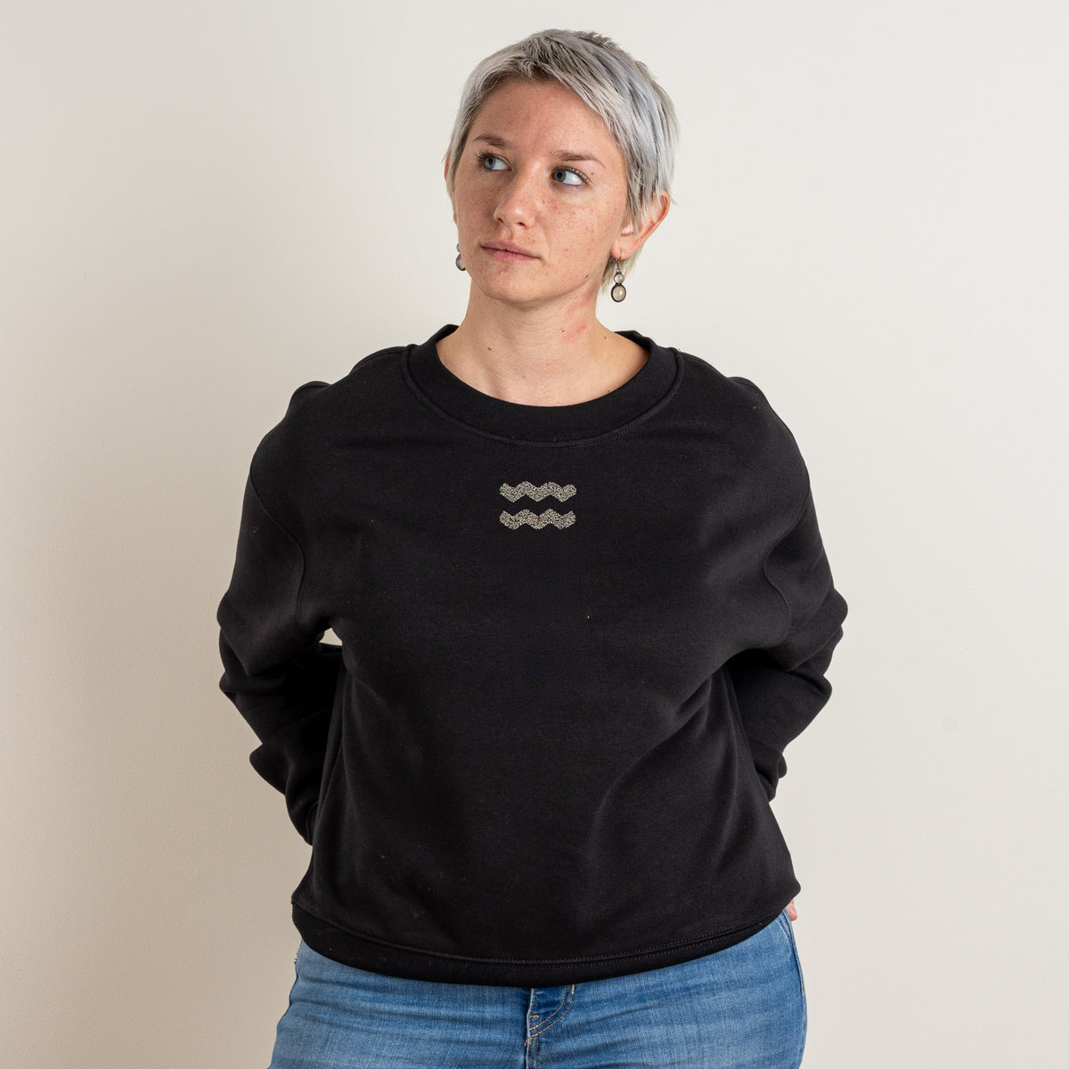 Woman wearing the black personalised Relaxed Sweatshirt with Aquarius embroidered on the centre chest in grey thread