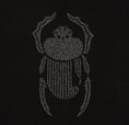 Load image into Gallery viewer, Macro detail of grey scarab embroidery on the Gordina black oversized cotton T-shirt.
