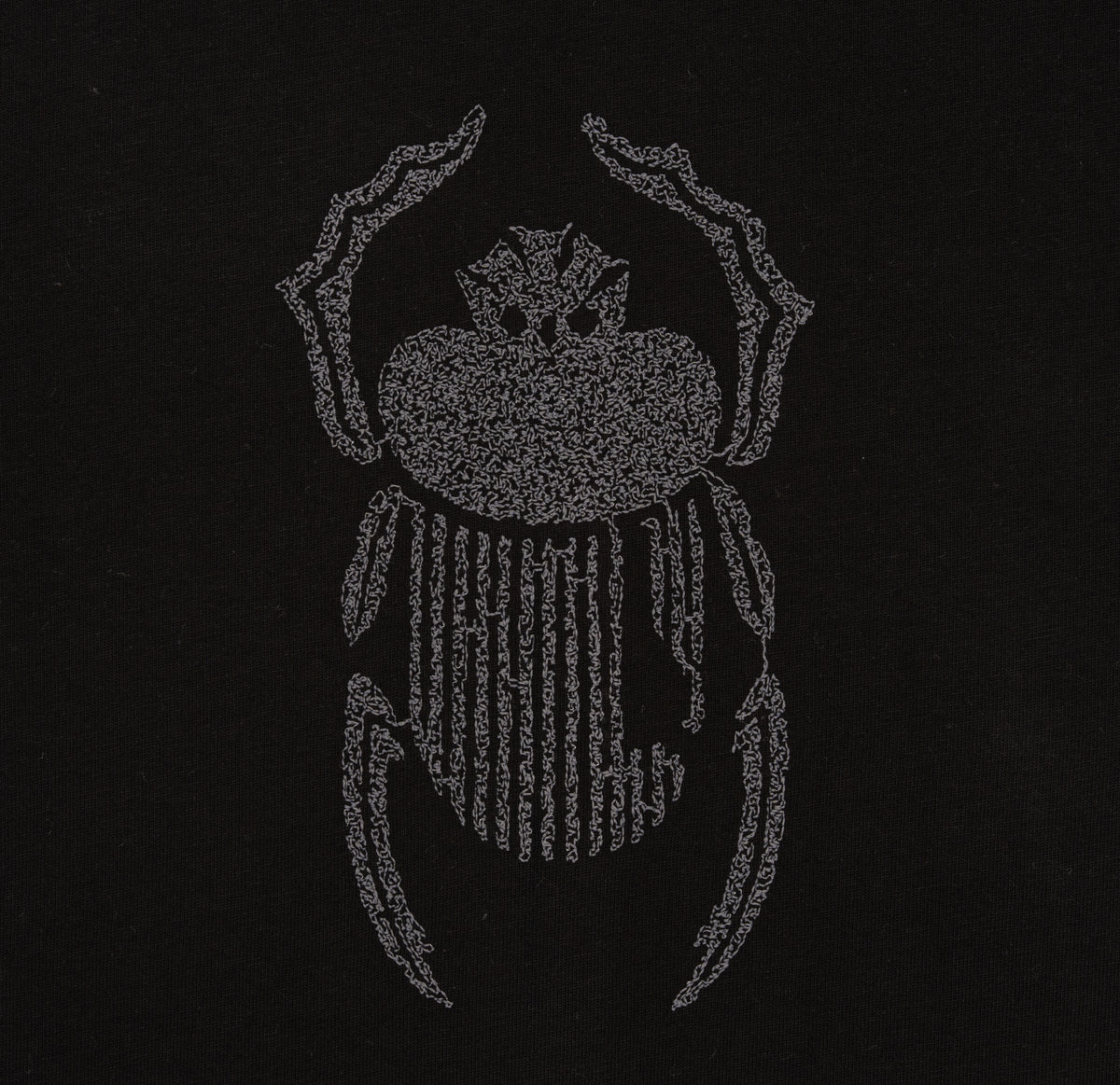 Macro detail of grey scarab embroidery on the Gordina black oversized cotton T-shirt.