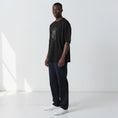 Load image into Gallery viewer, Front view of a model wearing the Gordina The Scarab black oversized T-shirt with grey scarab embroidery.
