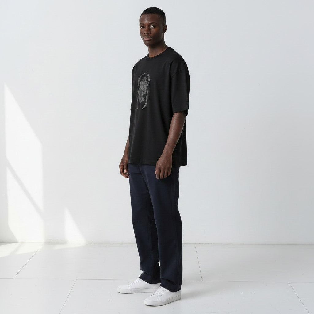 Front view of a model wearing the Gordina The Scarab black oversized T-shirt with grey scarab embroidery.