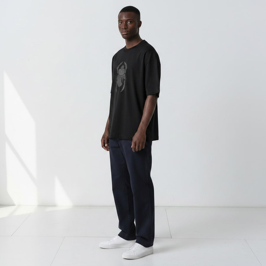 Front view of a model wearing the Gordina The Scarab black oversized T-shirt with grey scarab embroidery.