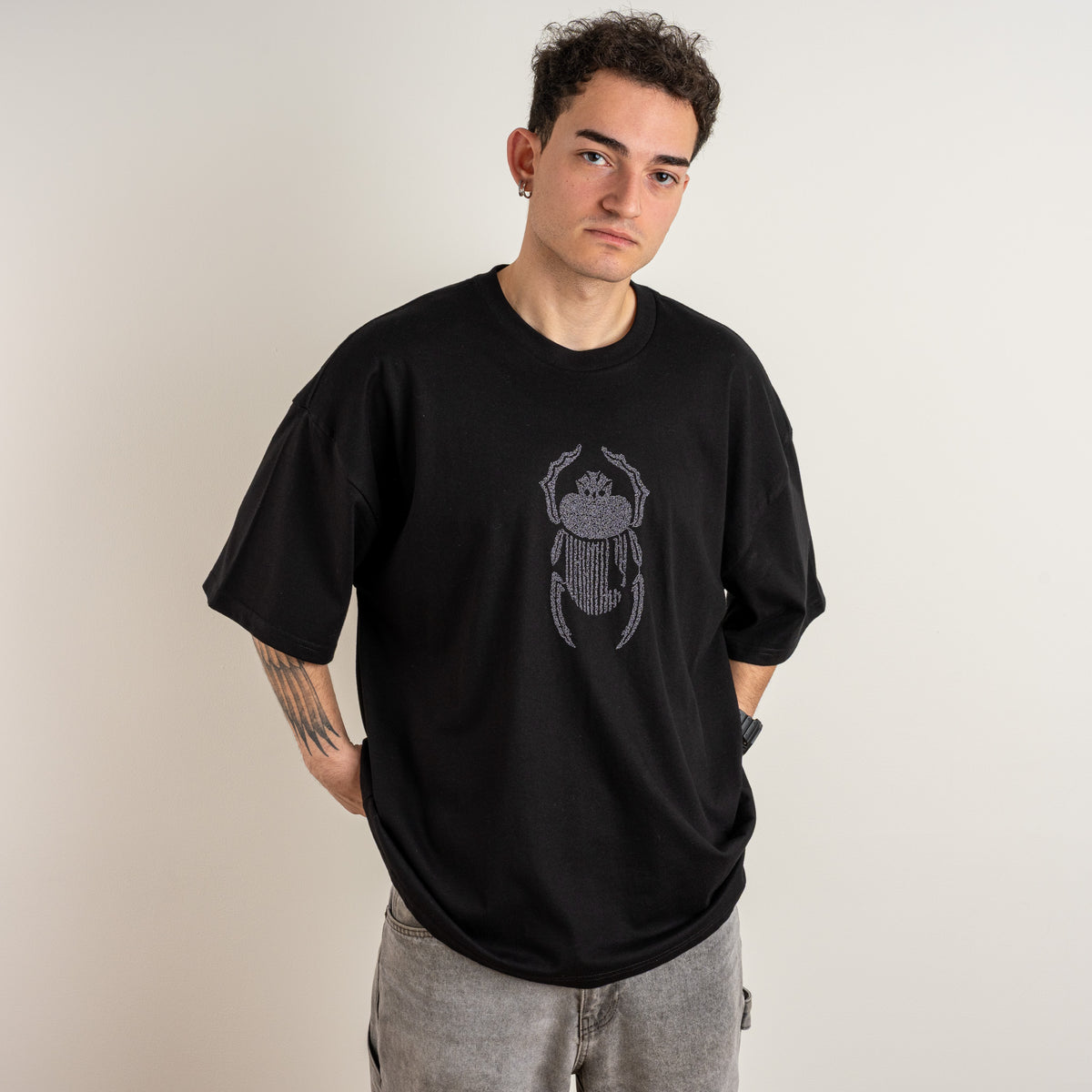 Model wearing the Gordina The Scarab black oversized T-shirt with grey scarab embroidery, front angled view.