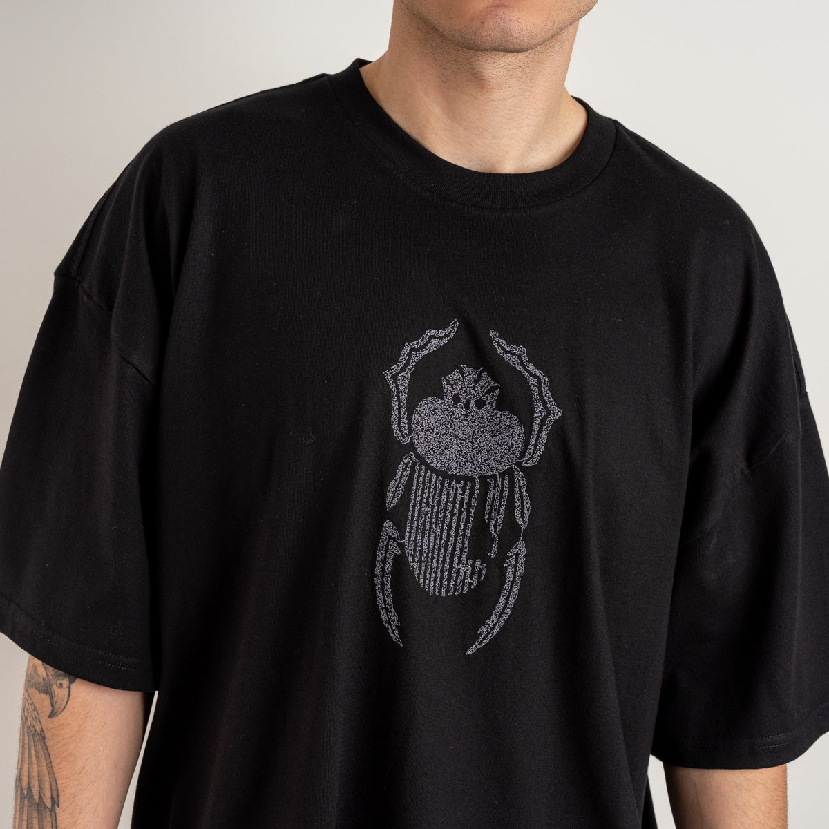 Close-up detail of grey scarab embroidery on the Gordina black heavyweight cotton T-shirt.