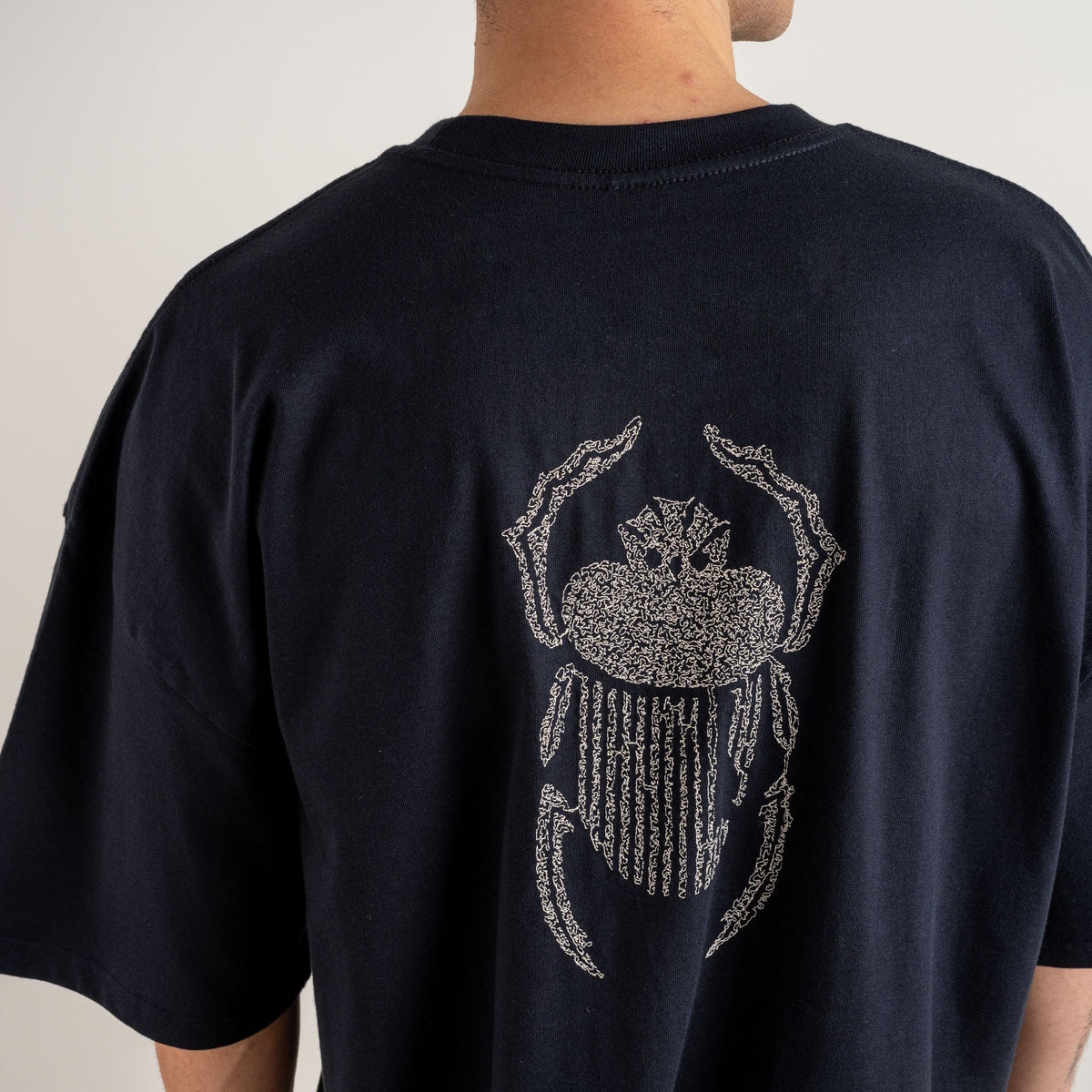 Close-up of ivory scarab embroidery stitched on the back of the Gordina The Scarab navy oversized T-shirt.