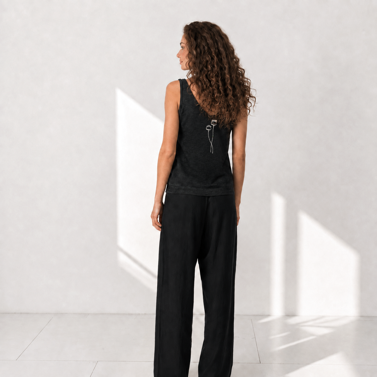 The Poppy Black linen tank top with cream poppy embroidery, model back view
