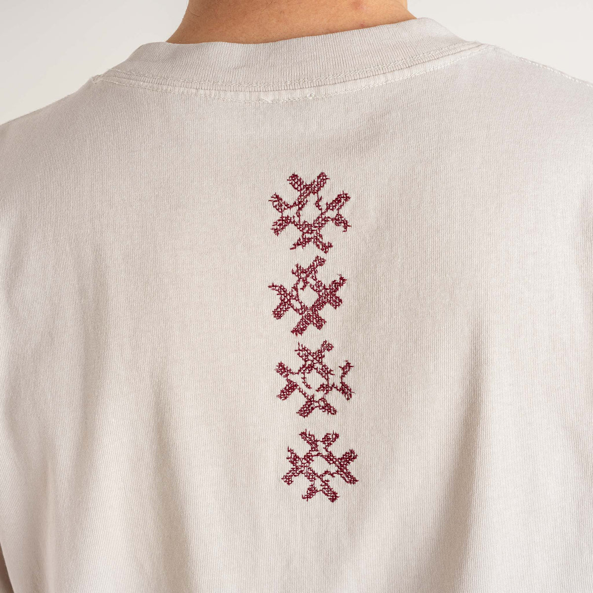 Detailed view of the vertical burgundy embroidered motif on the beige Gordina Unsigned cotton T-shirt, crafted in the Netherlands.