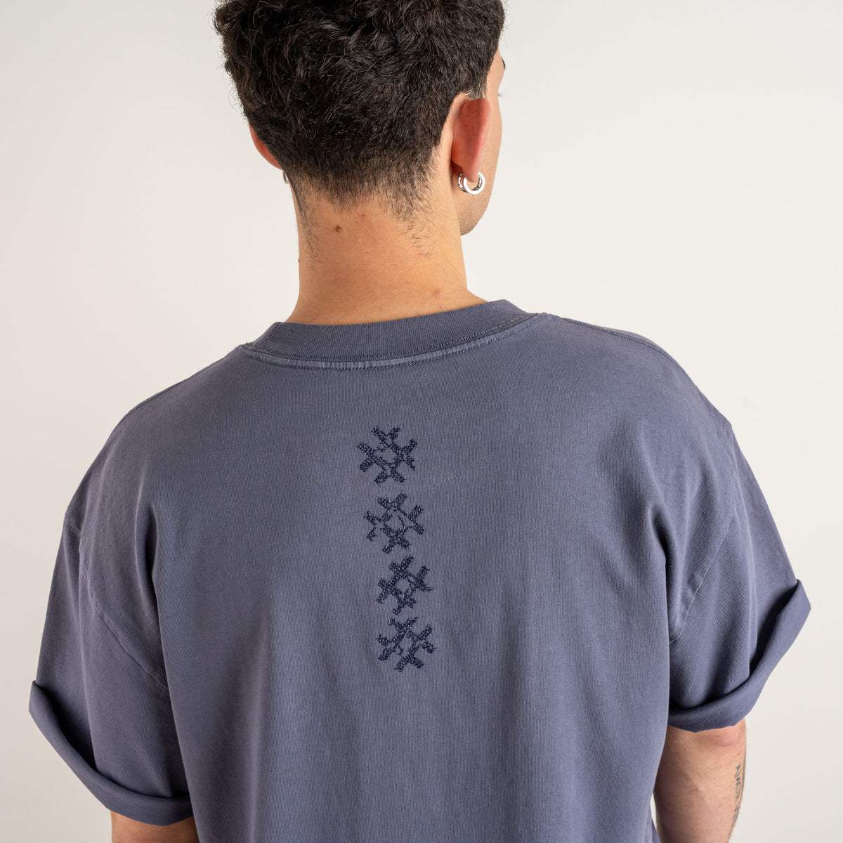 Close-up of the vertical navy cross embroidery on the faded indigo Gordina Unsigned T-shirt, crafted in the Netherlands.