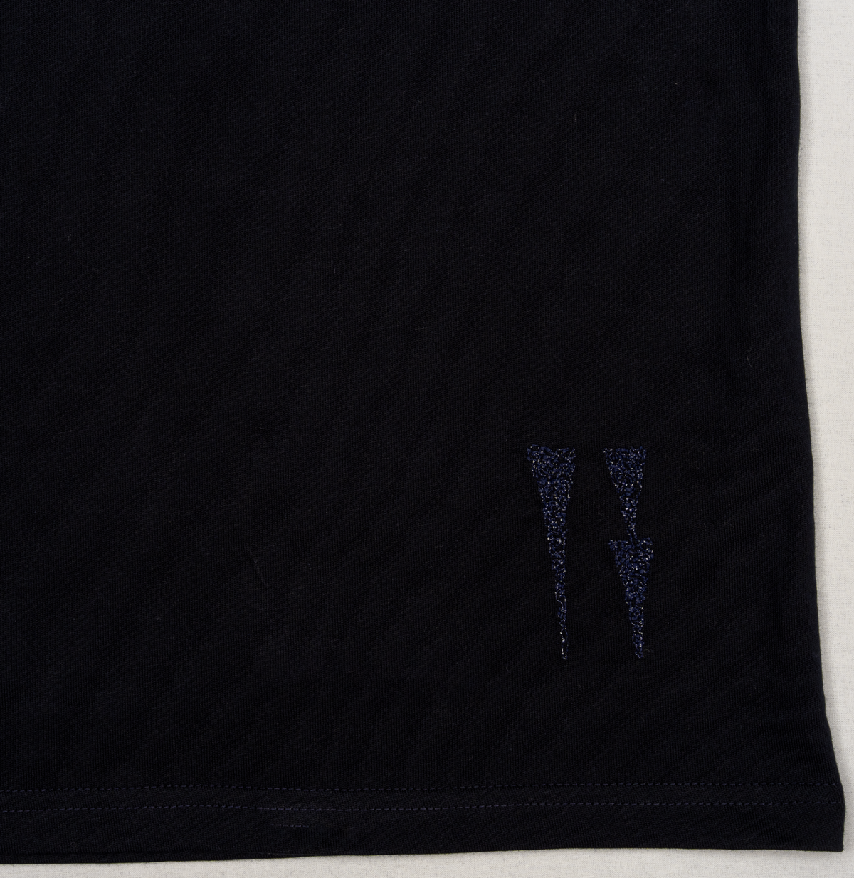 Close-up of the two embroidered water signs near the hem of the navy T-shirt.