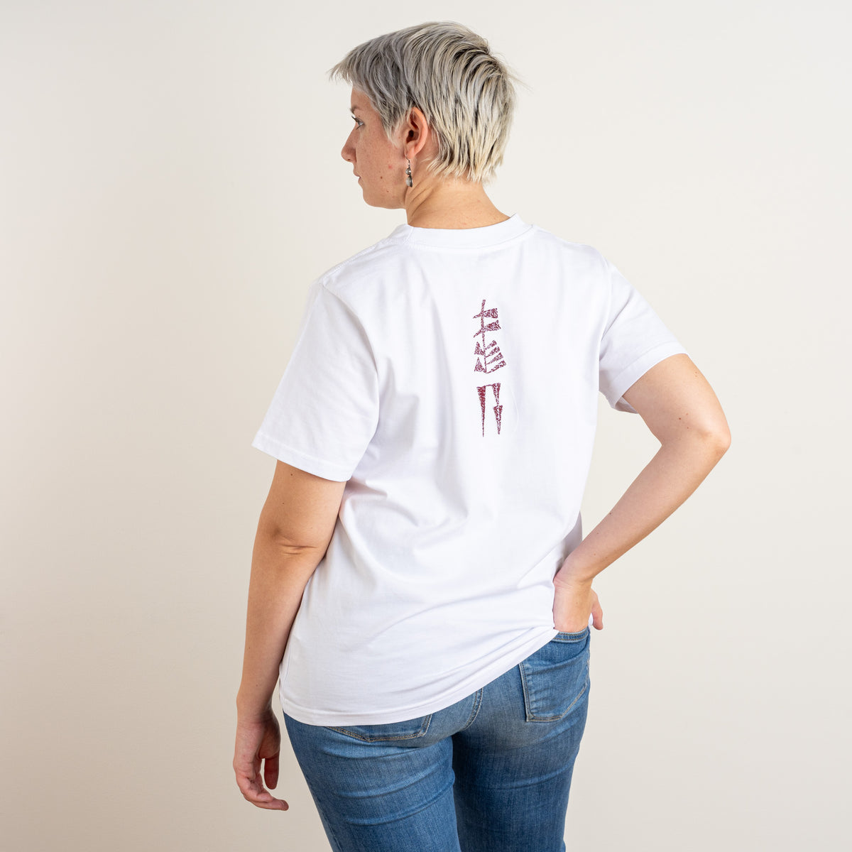 Three-quarter back view showing the burgundy Water and Garden embroidery on Gordina’s white women’s cotton T-shirt, made in the Netherlands.
