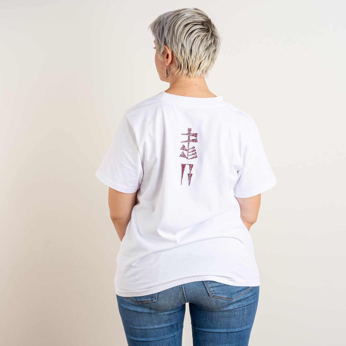 Back view of a woman wearing Gordina’s white T-shirt with burgundy Water and Garden cuneiform embroidery, embroidered in the Netherlands.