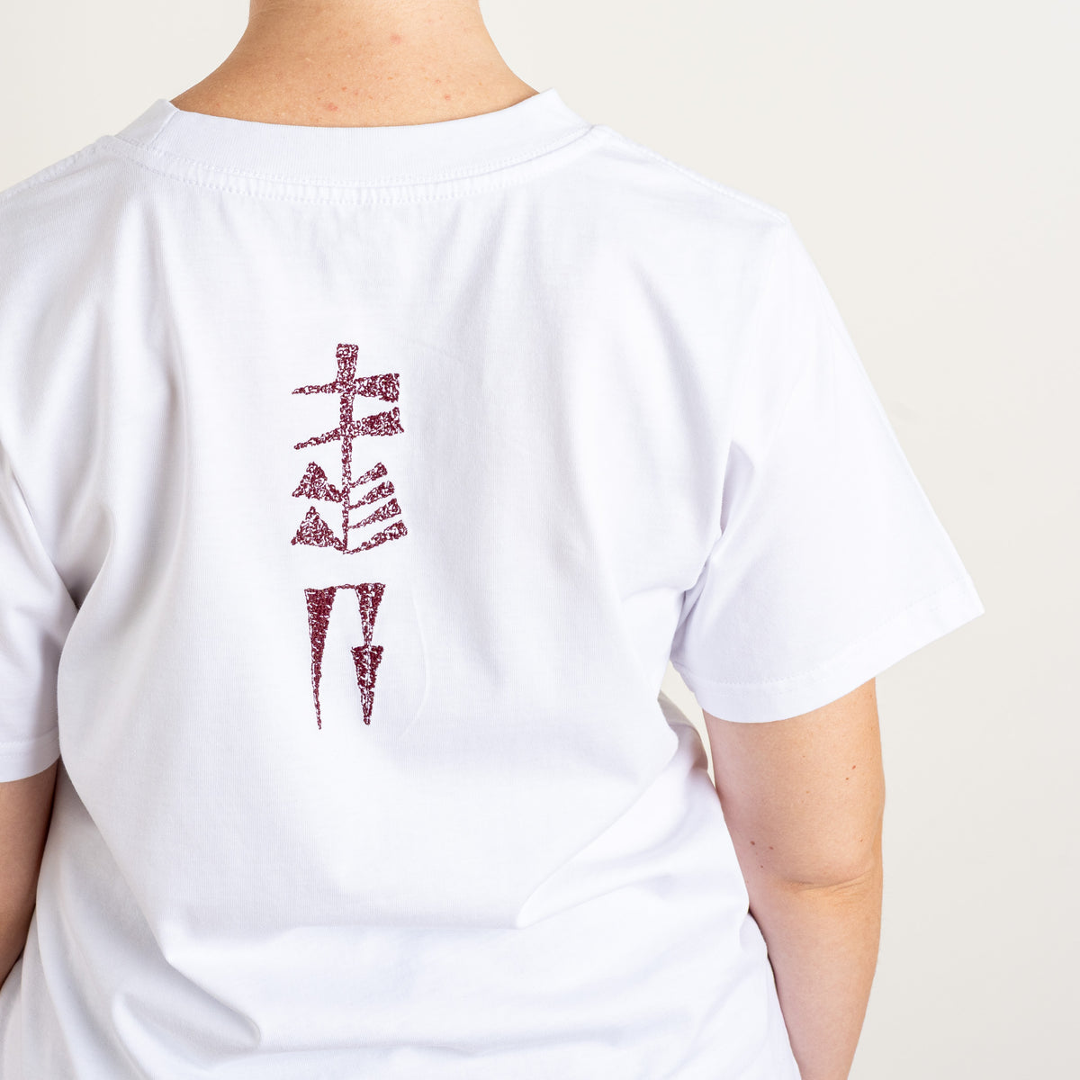 Close-up of the burgundy Water and Garden cuneiform embroidery stitched on the back of Gordina’s white cotton T-shirt.