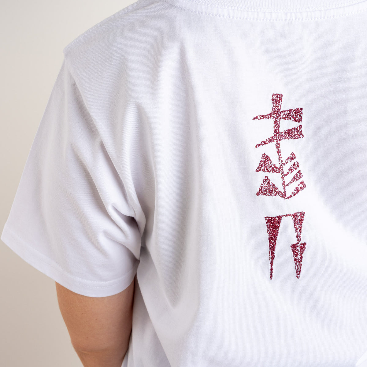 Detailed close-up of burgundy cuneiform embroidery on white cotton from Gordina’s Water and Garden T-shirt, embroidered in the Netherlands.