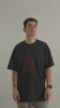 Model in a black oversized GORDINA T-shirt with a large dark-red embroidered scarab on the chest, against a plain wall.