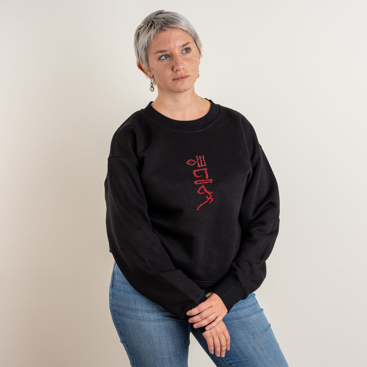 Model wearing the black Papyrus sweatshirt with red hieroglyphic-style embroidery