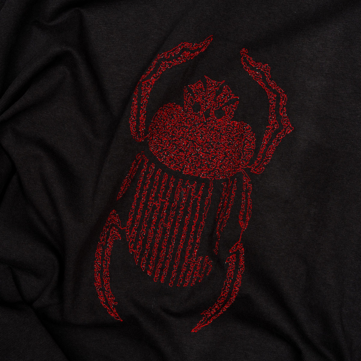 Angled close-up of red scarab embroidery on the black Gordina Scarab T-shirt.