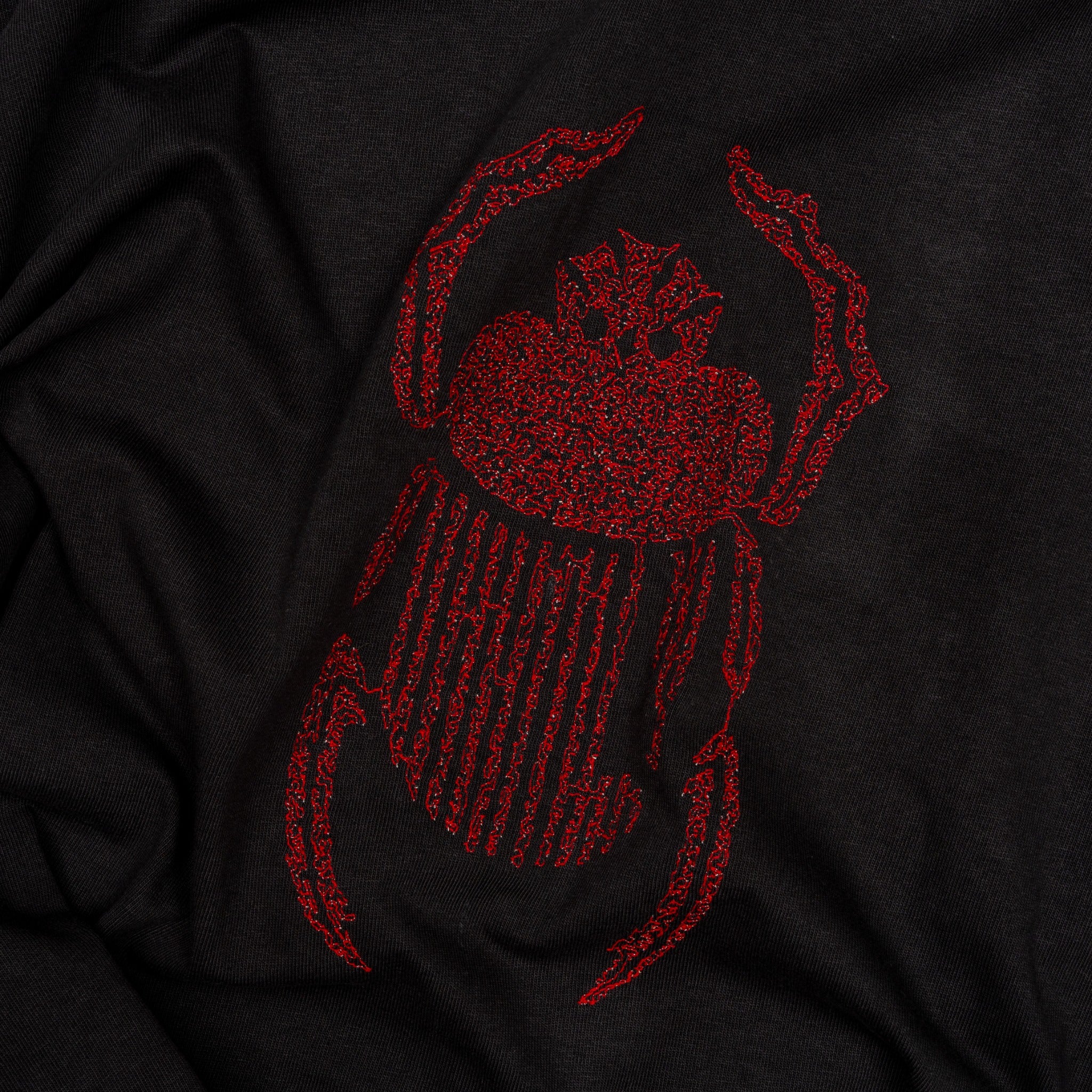 Angled close-up of red scarab embroidery on the black Gordina Scarab T-shirt.