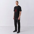 Load image into Gallery viewer, Three-quarter front view of a model wearing the black Gordina Scarab T-shirt with red embroidery.
