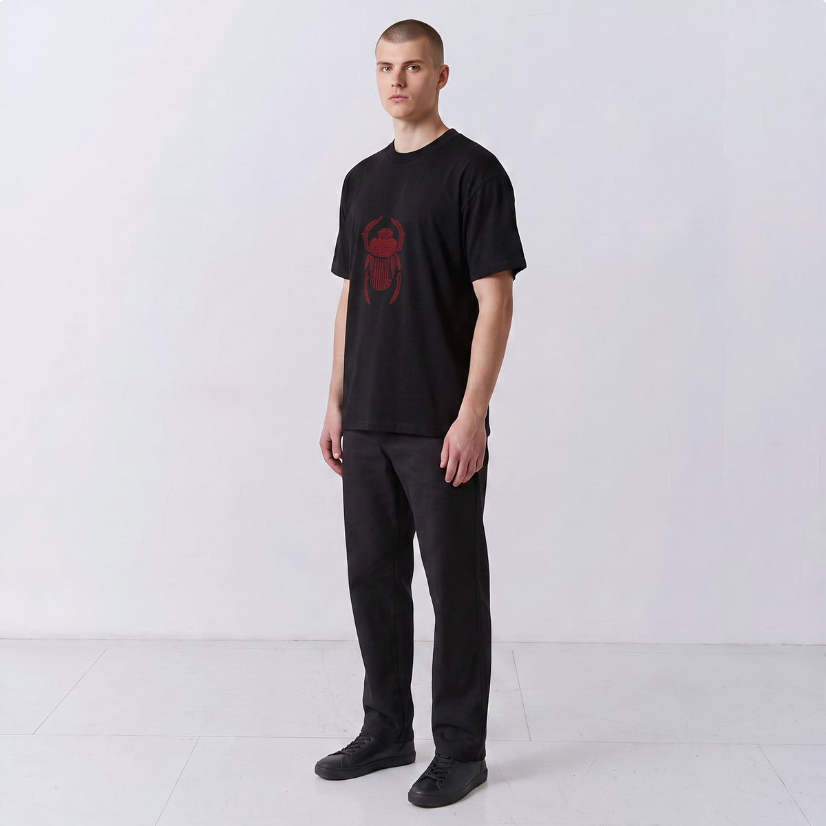 Three-quarter front view of a model wearing the black Gordina Scarab T-shirt with red embroidery.