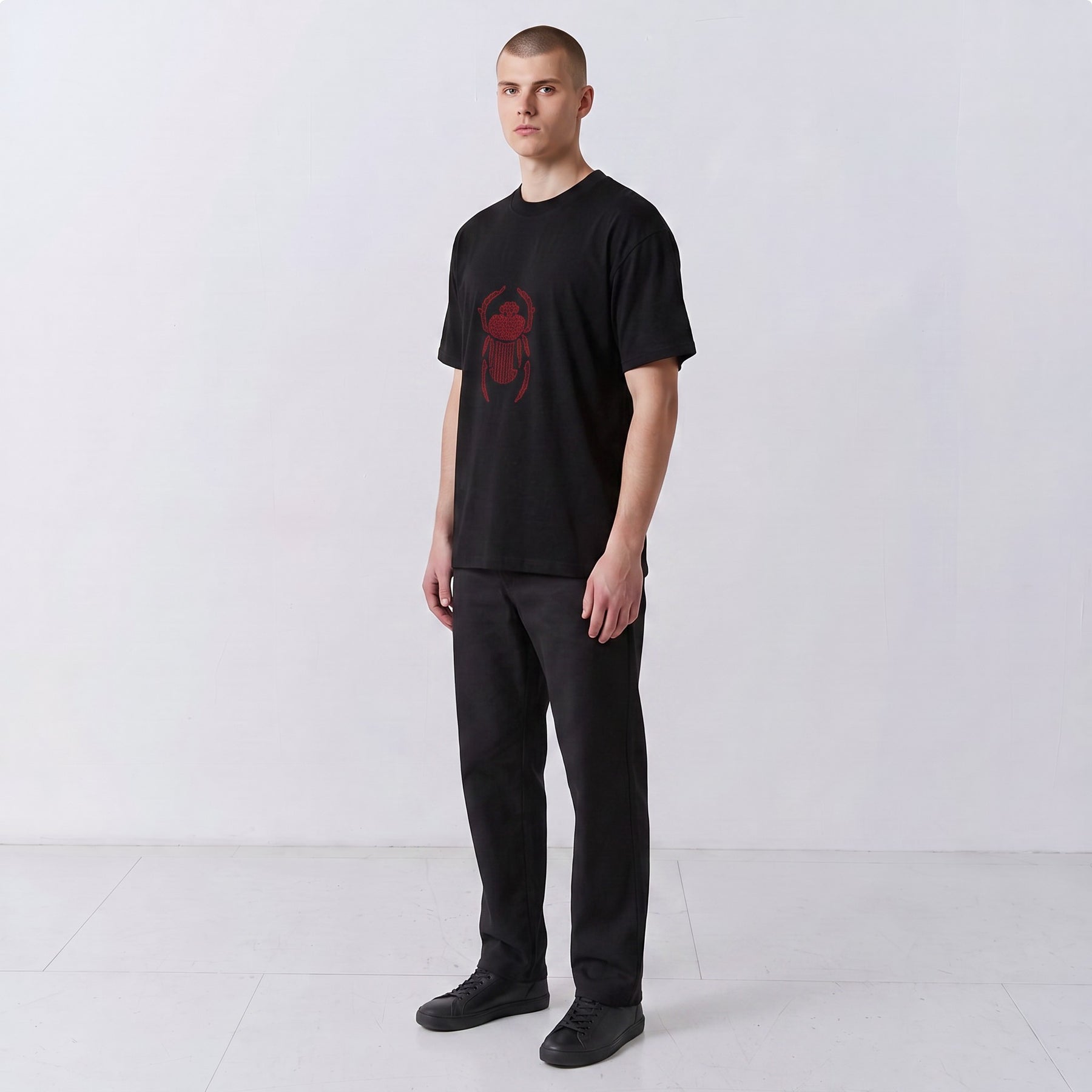 Three-quarter front view of a model wearing the black Gordina Scarab T-shirt with red embroidery.