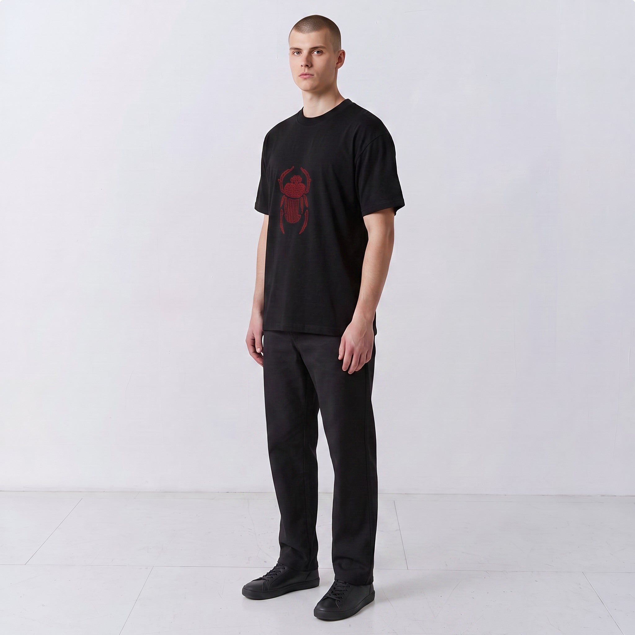 Three-quarter front view of a model wearing the black Gordina Scarab T-shirt with red embroidery.