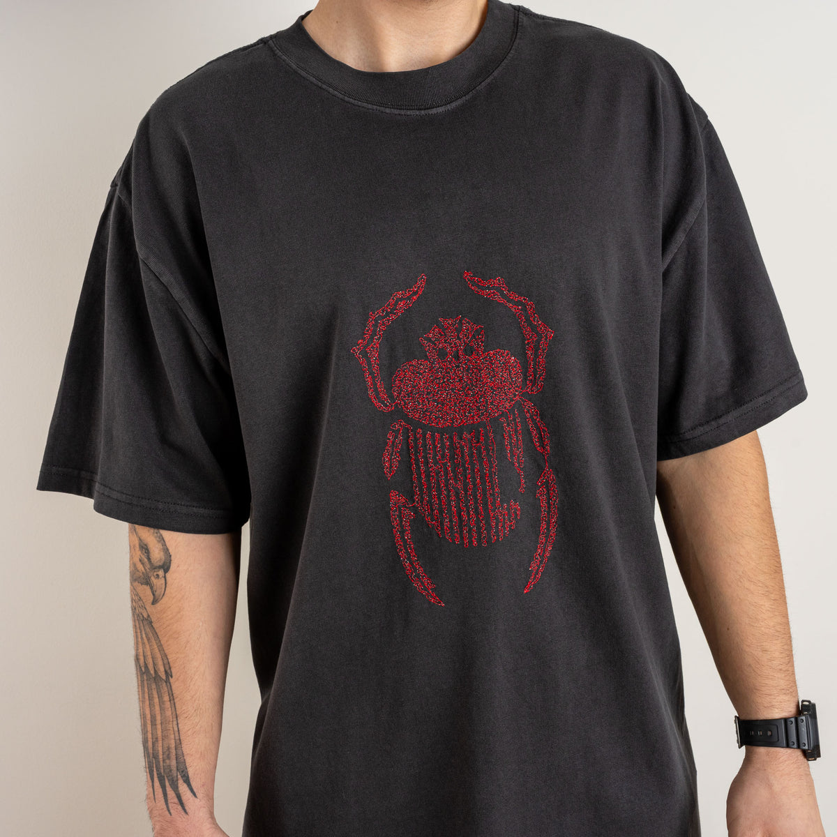 Close-up detail of red scarab embroidery on the faded black Gordina heavyweight cotton T-shirt.