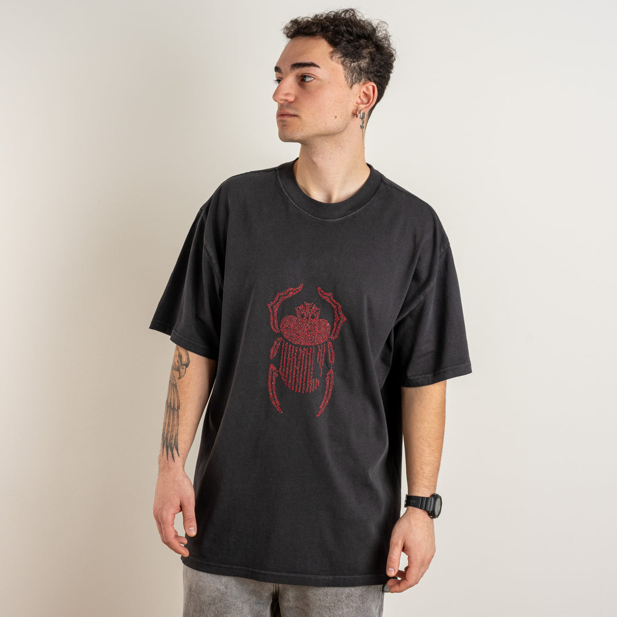 Front view of a model wearing the faded black Gordina Scarab T-shirt with red embroidery.