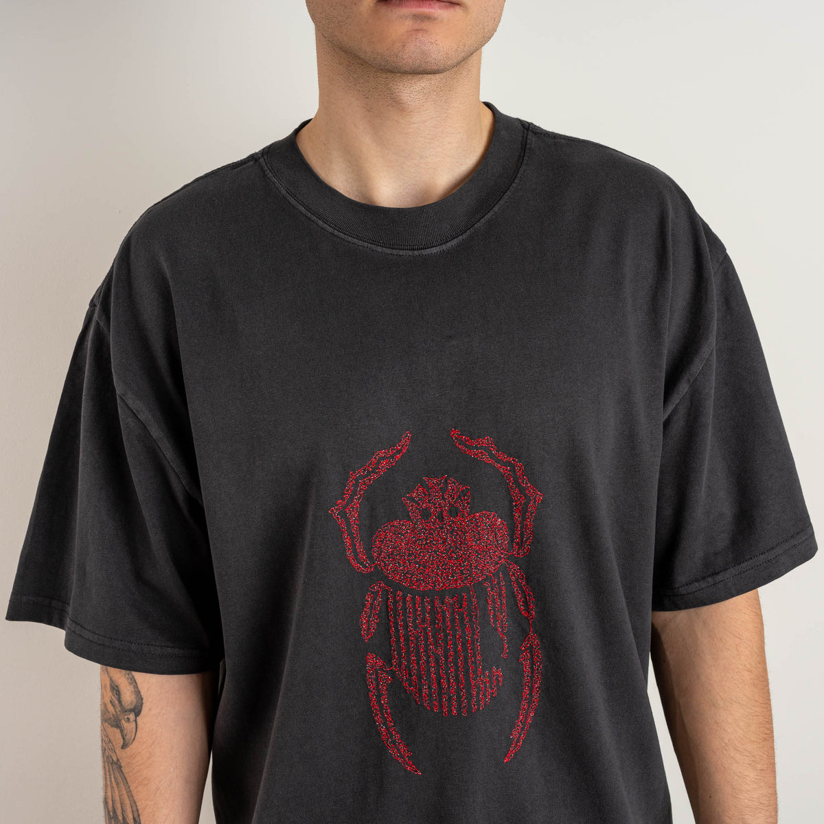 Detailed close-up of the red embroidered scarab motif on the front of the Gordina faded black T-shirt.