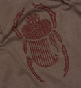 Afbeelding laden in Galerijviewer, Angled detail of burgundy scarab embroidery stitched onto faded grey cotton.
