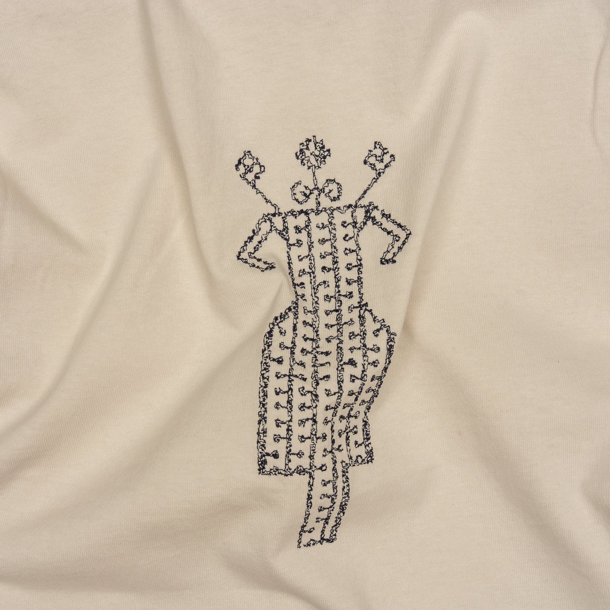 Close-up detail of black embroidery on The Ward Faded Bone T-shirt, with natural folds in the cotton.