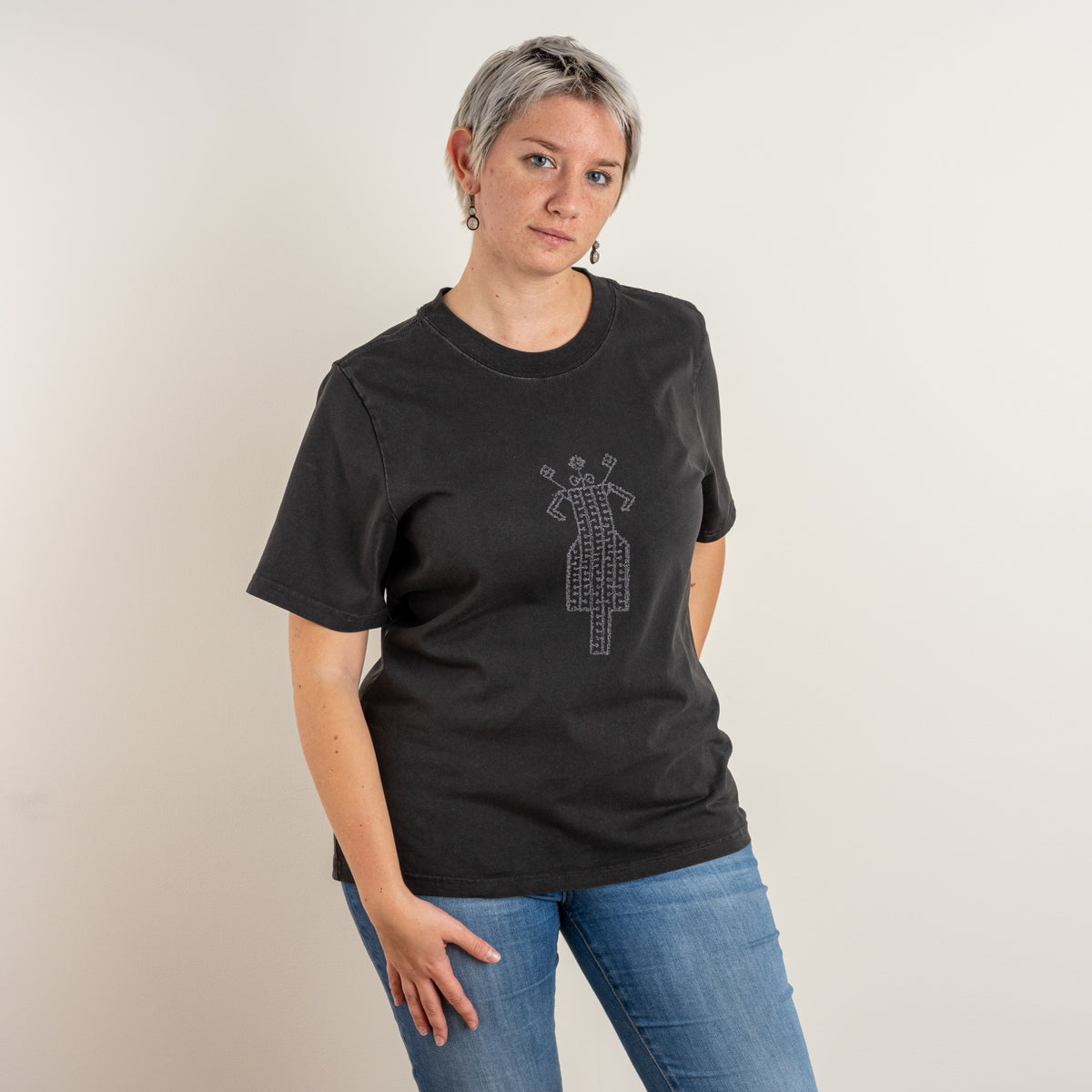Model wearing The Ward women’s Faded Coal embroidered T-shirt, shown from the front with the grey folk-inspired motif.