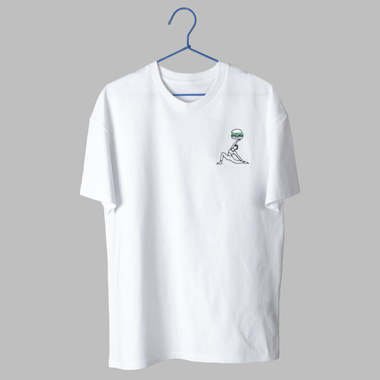 A white t-shirt on a blue wire hanger against a light grey background. It features a small embroidered design on the left chest of a black line-art figure in a side-plank yoga pose, balancing a large green and black hamburger on their raised hand.