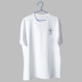 Load image into Gallery viewer, A white t-shirt on a blue wire hanger against a light grey background. It features a small embroidered design on the left chest showing a line-art figure sitting huddled over, with a flat line above them and a small green plant sprouting from the top.
