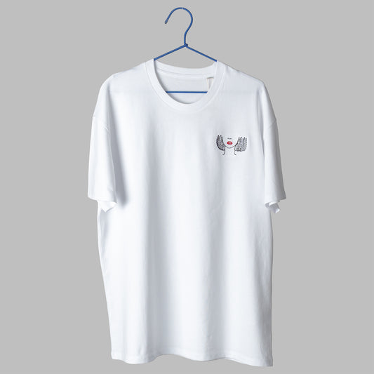 A white t-shirt on a blue wire hanger against a light grey background. It features a small embroidered design on the left chest showing the lower half of a face, including a nose, bright red lips, and a black line-art bob haircut.